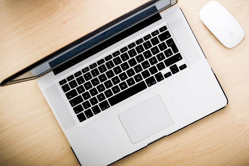 MacBook Pro seen from above showing its keyboard and trackpad, with a wireless mouse alongside